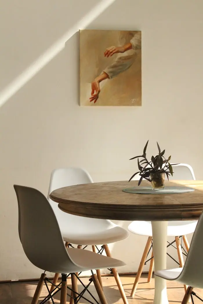 Sunlit minimalist dining room with round table, chairs, and painting.